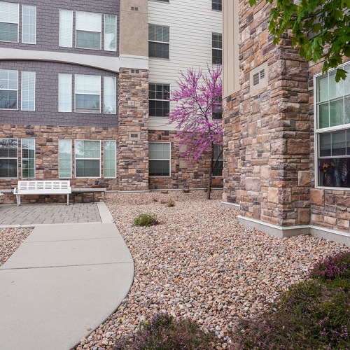 Outdoor court yard with lush landscaping The outdoor lounge at The Ivy at Draper 55 and over Apartments in Draper, UT, featuring a view of the apartment exteriors.